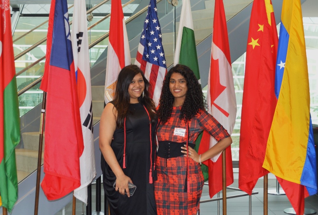 Two students in front of world flags smiling