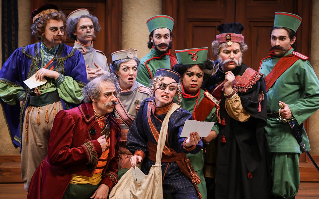 Acting students crowd around a woman holding a letter during a performance of The Government Inspector