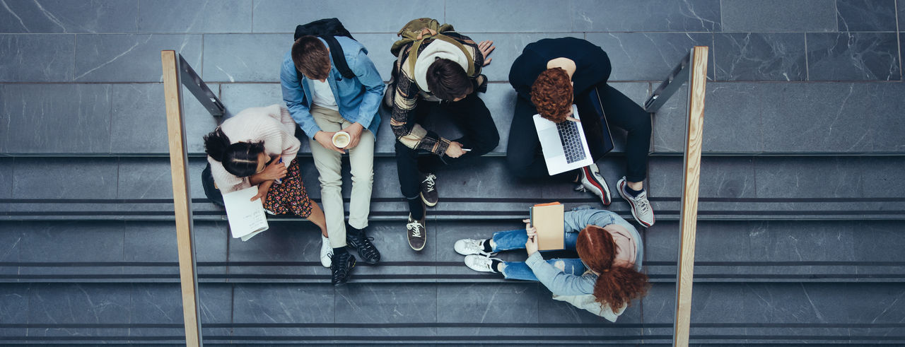Youngsters in university sitting on steps studying. Students sitting in college campus.